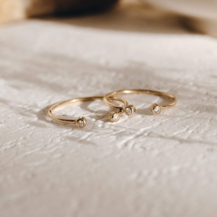 Three gold rings, resting on a textured surface, each featuring a single small diamond at the top.