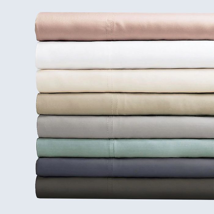 Stacked folded bed sheets resting on a reflective surface, exhibiting a gradient of colors from beige to blue against a light background.