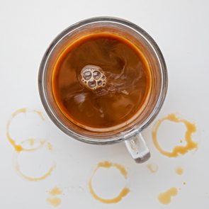 Coffee cup sitting still, surrounded by coffee ring stains on a white surface.