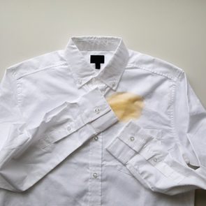 White shirt stained with a large coffee spill, lying on a plain, light-colored surface.