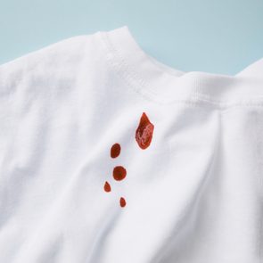 White shirt with red stains scattered on the surface, set against a light blue background.