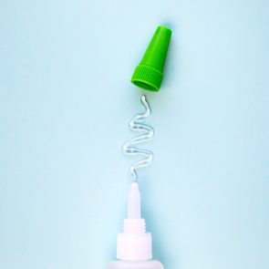 Bottle dispenses white liquid in a wavy line; green cap rests beside it on a light blue background.