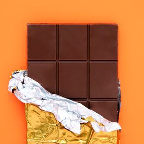 Chocolate bar, partially unwrapped, rests against an orange background.