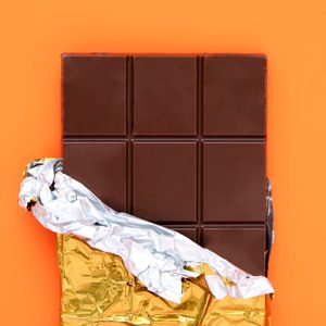 Chocolate bar, partially unwrapped, rests against an orange background.