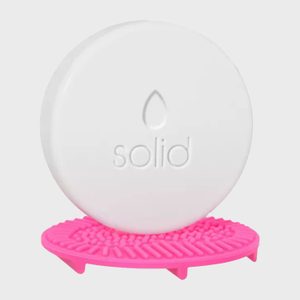 A white circular soap stands upright on a textured pink soap holder, with 
