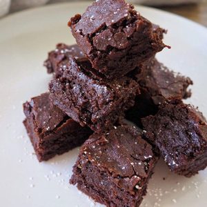 Brownie pieces stacked on a plate, dusted with powdered sugar, in a kitchen setting.