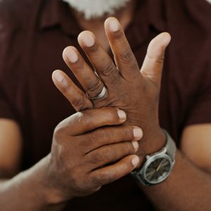 Hands clasped together, one wearing a ring and watch, in a casual setting.