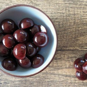 Shiny, dark brown spheres rest in a bowl on wooden table; some lie beside the bowl, creating a scattered arrangement.