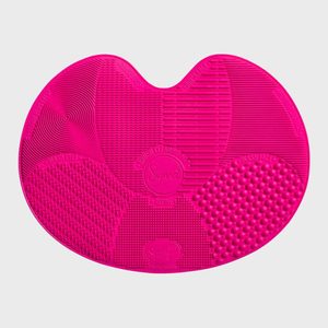 Pink silicone mat displaying various textured surfaces with labeled sections for washing and rinsing. Circular patterns and grid designs cover the mat's surface.