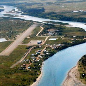 Aerial view of a rural airstrip; surrounded by a river, scattered buildings, and dense greenery.