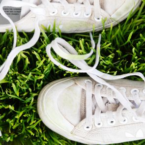 White sneakers lie on vibrant green grass, with laces untied and text 