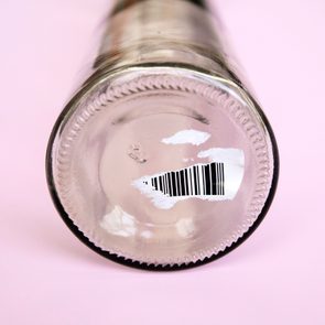 Glass bottle features a barcode sticker, resting on a pink surface.