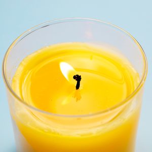 Yellow candle burns in a glass holder, casting light against a soft blue background.
