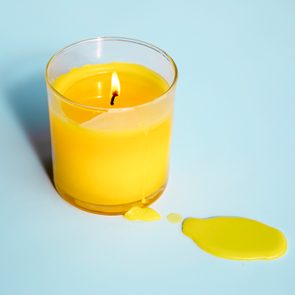 Yellow candle burns, wax drips onto light blue surface.