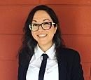 A person, wearing glasses and a suit, smiles against a red background.