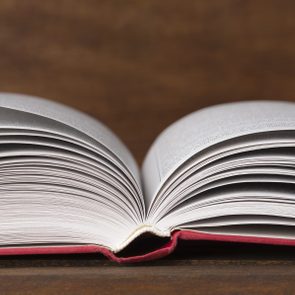 Open book lying flat, pages slightly fanned, resting on a wooden surface in a warm, dimly lit environment.