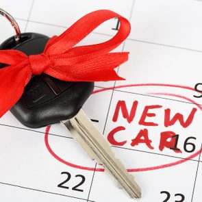 A car key with red bow rests on a calendar. The calendar highlights the phrase 