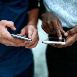 Hands holding smartphones point at screens, engaged in activity, with casual clothing visible in an outdoor setting.