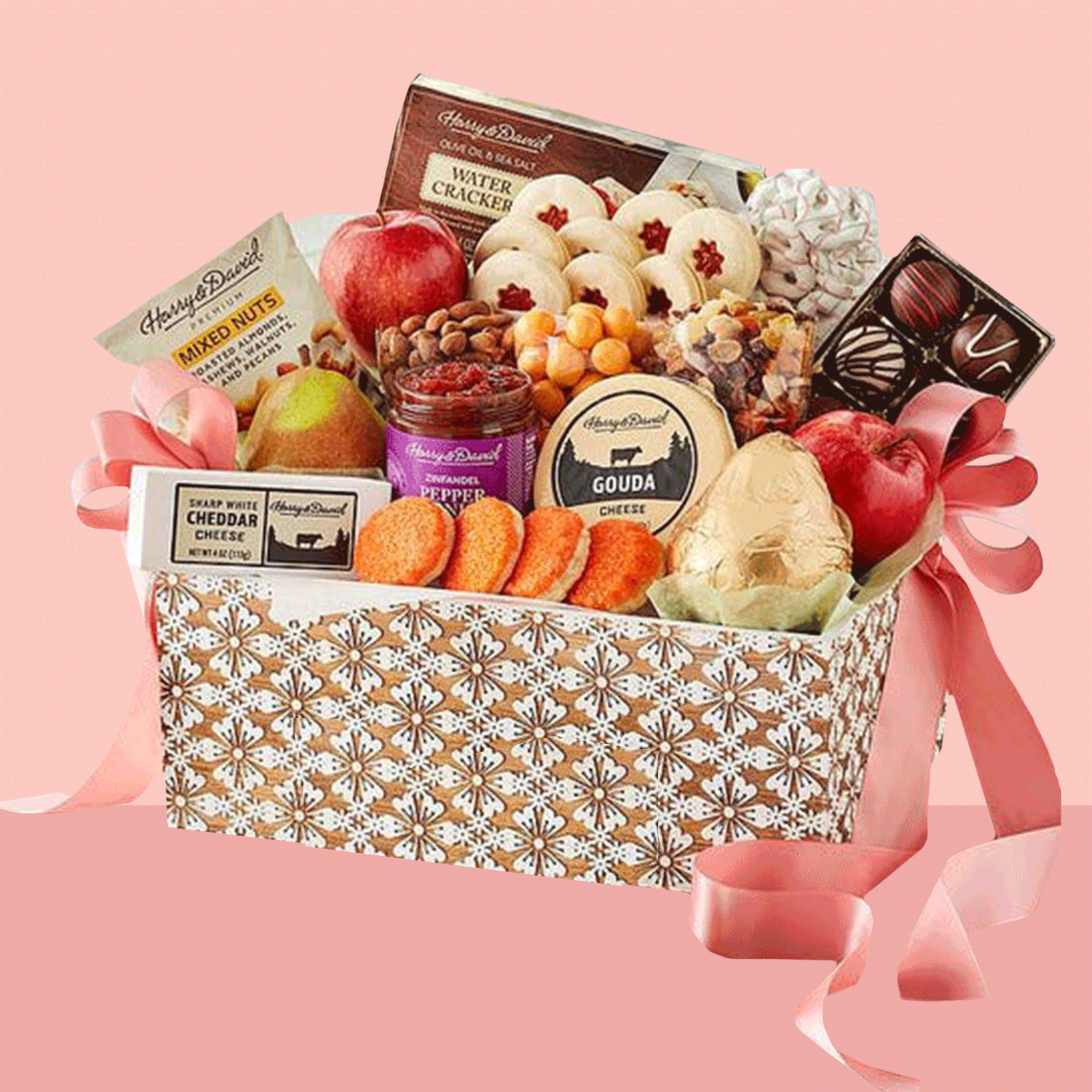 Gift basket holds assorted snacks and fruits, wrapped with a pink ribbon, set against a plain pink background.