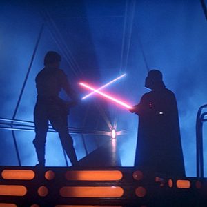 Two figures wielding lightsabers clash dramatically on a platform, surrounded by blue mist and backlit by intense light.