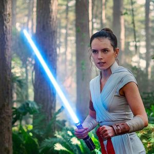 A person wields a glowing blue lightsaber amidst a dense, sunlit forest.