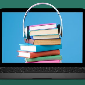 Headphones rest on a stack of colorful books displayed on a laptop screen, against a blue background.