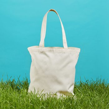 A beige tote bag stands on green grass, set against a solid blue background.