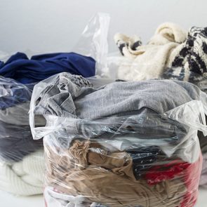 Plastic bags hold assorted folded clothes, resting on a white surface, against a plain background.