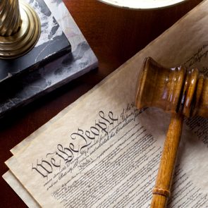 A wooden gavel rests on the U.S. Constitution, partially visible text reads 