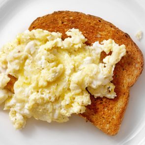 Scrambled eggs rest on toasted bread, served on a white plate.
