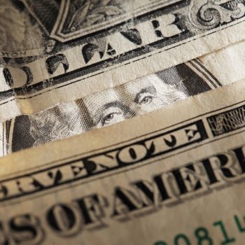 Dollar bills layered closely, showing partial text and a person's eyes, in a detailed close-up view.