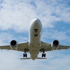 Airplane flies with landing gear extended, set against a cloudy blue sky.