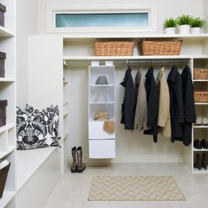 Closet contains hanging coats, hats, and gloves, with baskets and decorative items neatly arranged on white shelves, creating an organized and tidy space.