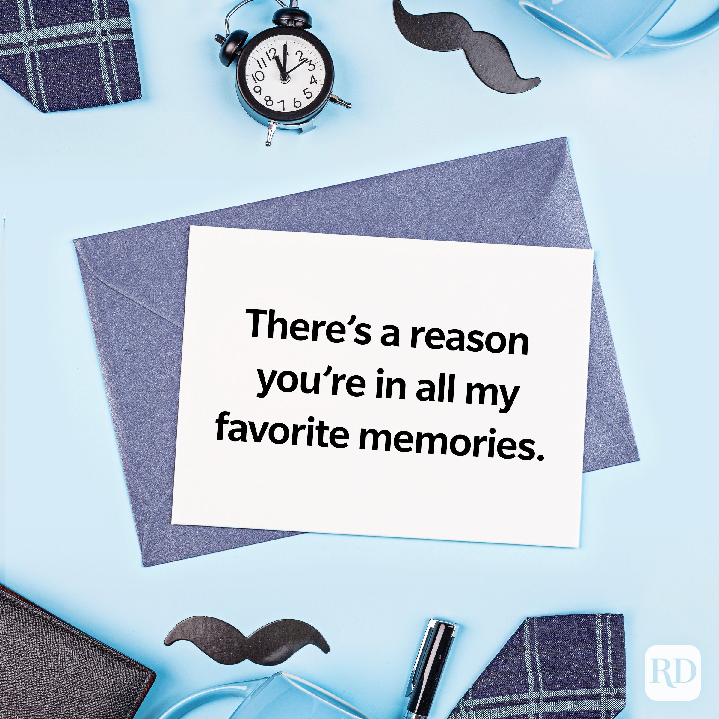 Card rests on envelopes, expressing sentiment: "Thereâ€™s a reason youâ€™re in all my favorite memories." Surrounded by a clock, pen, mustache cutouts.