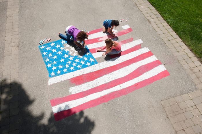 Girls with chalk coloring American flag on sidewalk