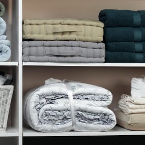 Shelves display neatly folded towels, stacked blankets, and a basket of toiletries in a closet.