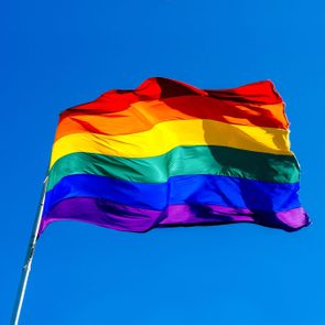Rainbow flag waves vibrantly against a clear blue sky.