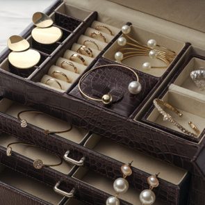 Jewelry is neatly organized in a textured brown box with earrings, rings, and bracelets placed in individual compartments on a beige interior.