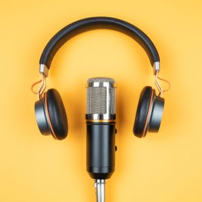 A microphone stands upright, framed by headphones, on a bright yellow background.