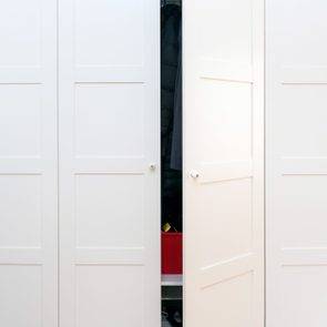 White wardrobe door slightly open, revealing clothes inside and a red box. The setting is a minimal, tidy room.