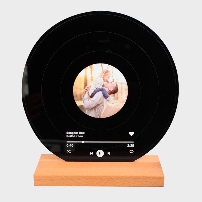 Record-style photo display with a circular frame shows a father holding a child, resting on a wooden base. Text reads: 