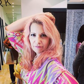 Person poses with hand on head, wearing a colorful patterned top in a modern indoor setting.