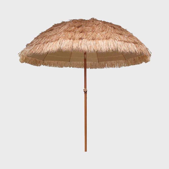 A thatched patio umbrella stands upright against a plain, light gray background.
