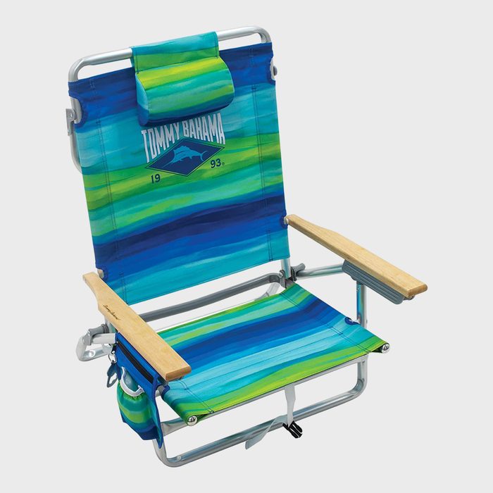 Beach chair displays vibrant blue-green stripes, text â€œTommy Bahamaâ€ with a logo, includes a padded headrest and wooden armrests, set against a plain backdrop.