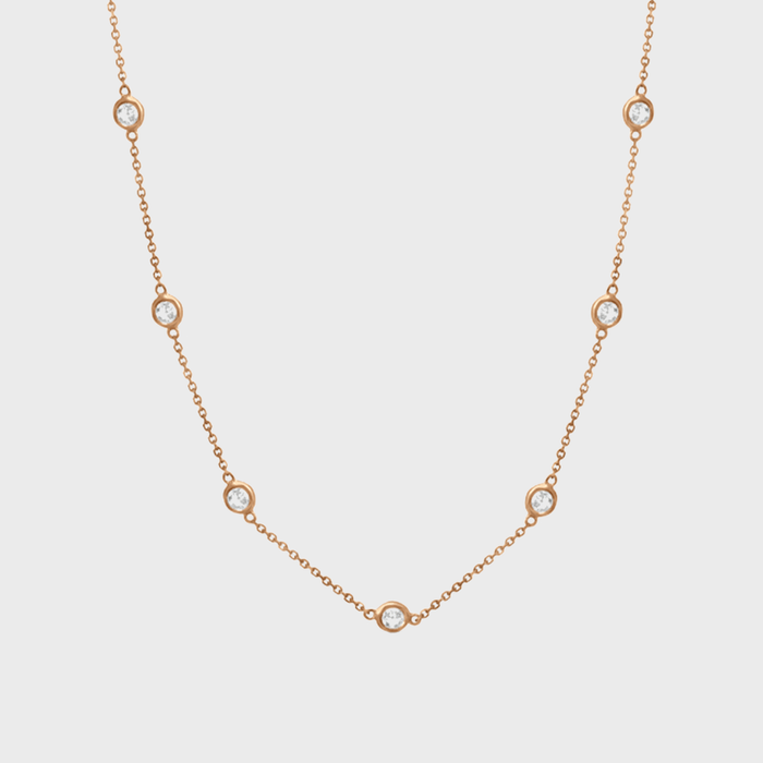 A gold chain necklace displays evenly spaced circular diamond-like stones, elegantly positioned against a plain white background.