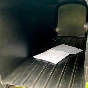 Envelope lies inside an open black mailbox with a red flag, outside in a grassy area.