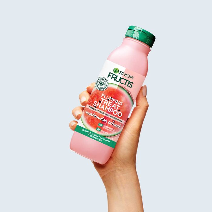 A hand holds a pink Garnier Fructis shampoo bottle, labeled 
