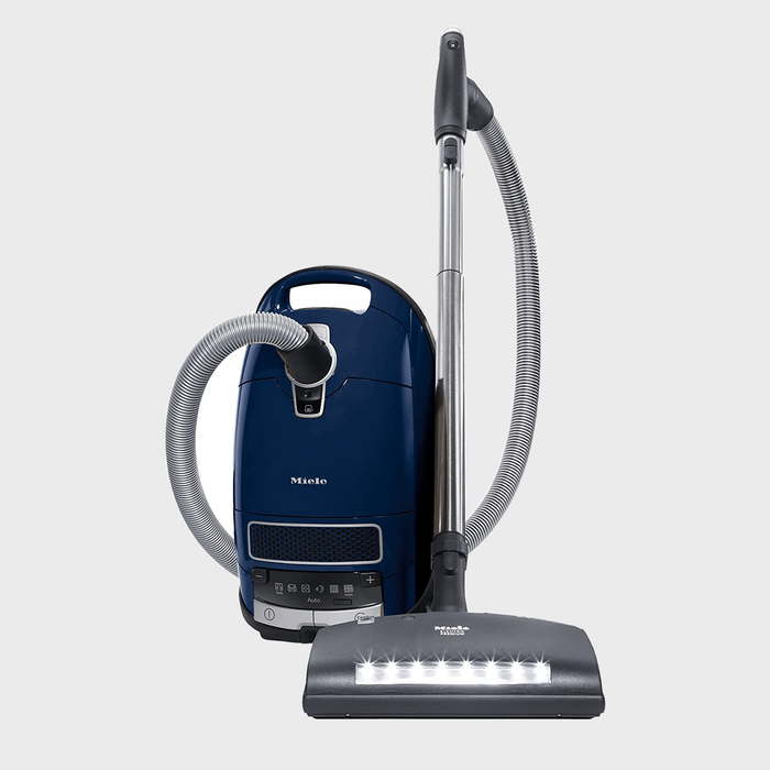 Vacuum cleaner stands upright, featuring retractable hose and LED-lit nozzle, against a plain background. The brand 