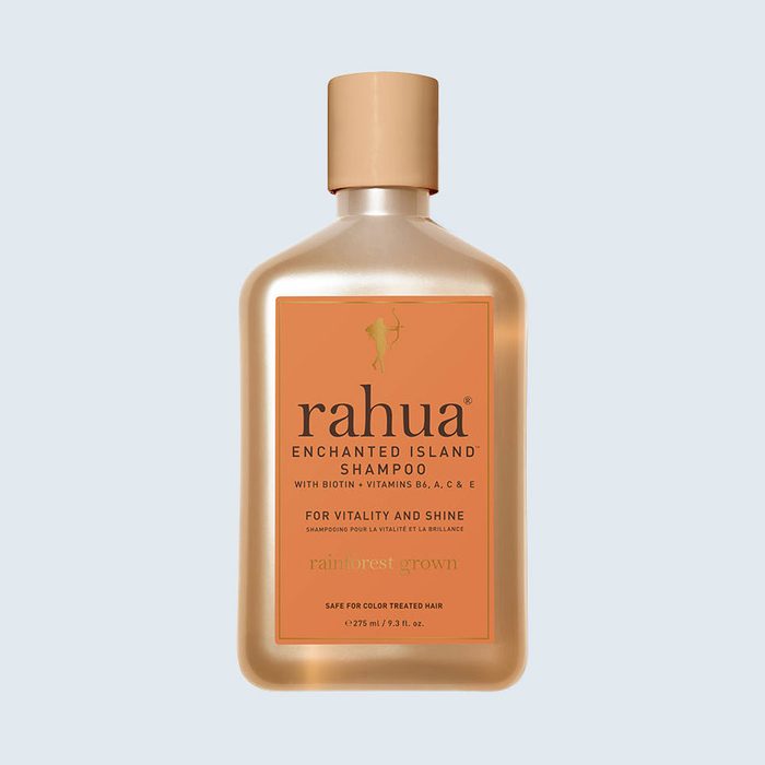 Shampoo bottle stands against a plain background. It features orange labeling with text: 