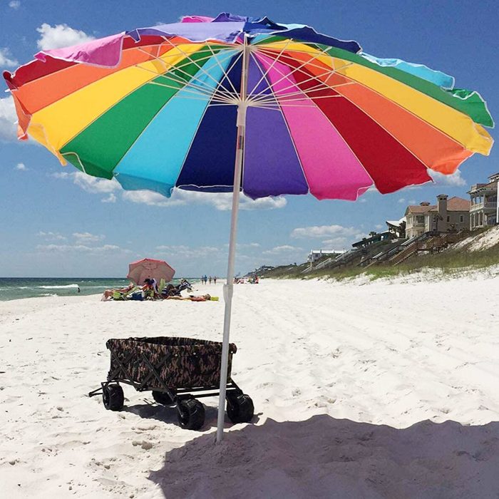 Colorful umbrella shading cart on a sunny beach with houses and people in the background.
